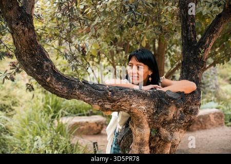 Nachdenkliche Frau, die sich auf Baumzweige im grünen Garten lehnt Stockfoto