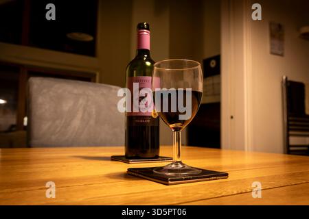 Eine Flasche chilenischer Merlot und ein halbes Glas auf einem hölzernen Esstisch. Stockfoto