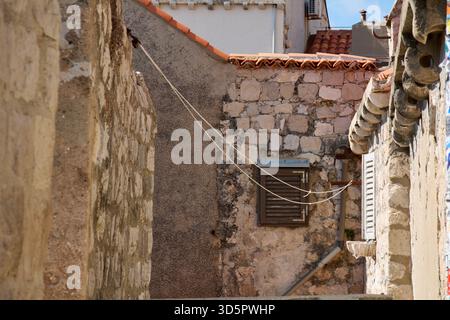 Sonnenlicht beleuchtet die historische Architektur einer abgeschiedenen Gasse. Der verwitterte Stein, die Holzblende und die Terrakottafliesen schaffen eine zeitlose Reise Stockfoto