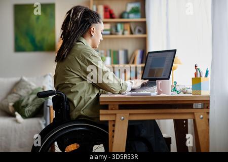 Junge Erwachsene Frau mit Behinderung, die bei der Arbeit von zu Hause aus mit einem Laptop arbeitet Stockfoto