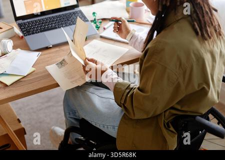 Junge Erwachsene Frau mit Behinderung, die Dokumente am Schreibtisch überprüft Stockfoto