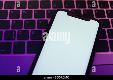 Schicke Nahaufnahme des Smartphones, das auf der Laptop-Tastatur liegt, mit Neonbeleuchtung, minimalem Mockup für die App-Präsentation. Kopierbereich für digitale Werbung oder kreative Vorlage. Stockfoto