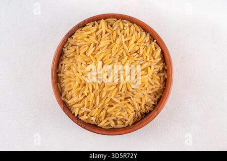 Rohe, ungekochte Orzo-Nudeln, italienische trockene Nudeln Risoni Orzo in Schüssel auf dem Tisch, Kopierraum Stockfoto