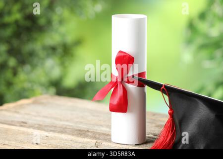 Graduierungskappe und Diplom auf Holztisch vor verschwommenem Hintergrund, Nahaufnahme. Leerzeichen für Text Stockfoto
