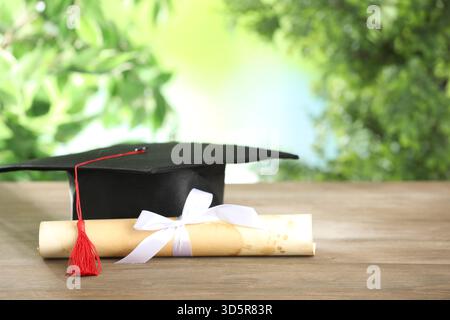 Graduierungskappe und Diplom auf Holztisch vor verschwommenem Hintergrund, Nahaufnahme. Leerzeichen für Text Stockfoto