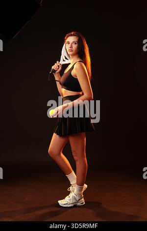 Tennisspielerin posiert selbstbewusst mit Schläger und Tennisball im Studio Stockfoto