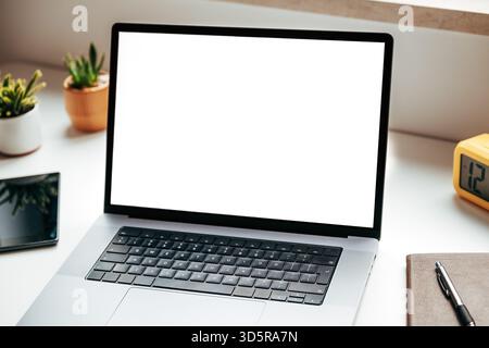 Offener Laptop mit leerem Mockup-Bildschirm auf weißem Bürotisch neben Notebook, digitalem Tablet und Kaktuspflanzen, modernes Arbeitsplatzkonzept. Selektiv Stockfoto