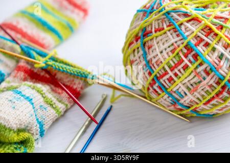 Wollgarn, buntes Strickprojekt und im Vordergrund angeordnete Nadeln, in Nahaufnahme dargestellt und ideal zum Basteln, Handarbeiten und Handma Stockfoto