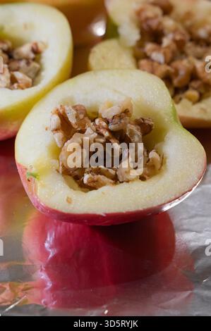 Apfelhälften gefüllt mit Walnussgranola, mit Zimtzucker glasiert, auf zerknitterter Folie ruhen, Nahaufnahme mit Hafer- und Nussstücken, warmer Bernsteinfeucht Stockfoto