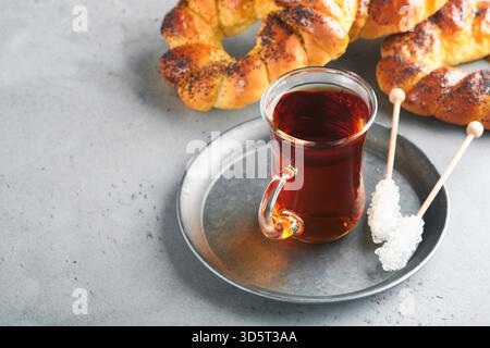 Türkischer schwarzer Tee. Eine Glasschale türkischer schwarzer Tee und knuspriger türkischer traditioneller Bagel auf grauem Betontischhintergrund. Frühstücksgebäck-Konzept. Traditionelles türkisches Heißgetränk. Stockfoto