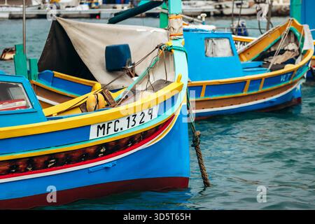 Marsaxlokk, Malta - 13. April 2025: Traditionelle, farbenfrohe maltesische Fischerboote namens Luzzu mit hellblauen, gelben und roten Details, die im malerischen Hafen von Marsaxlokk ankern Stockfoto