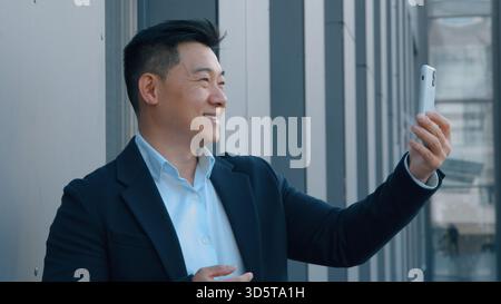 Asiatischer Geschäftsmann spricht Videoanruf in der Stadt mit Handy Chat koreanischer 40er Geschäftsmann männlicher Talk Online-Internetkonferenz mit Smartphone Stockfoto