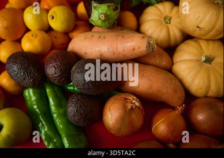 Ein lebhaftes Herbstangebot mit Süßkartoffeln, Avocados, Kürbissen, Zwiebeln, Paprika, Zitronen und Äpfel, in einer bunten Marktszene angeordnet Stockfoto