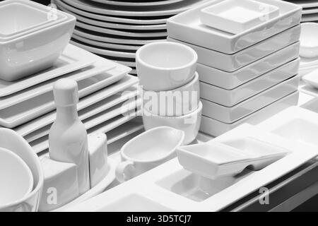 Ein Stapel weißer Teller und Schüsseln. Eine Schüssel liegt auf einem Stapel Teller. Restaurant Geschirr vor Tisch, Hotelrestaurant Service Konzept. Stockfoto
