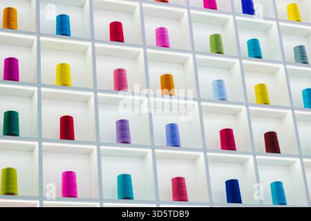 Spulen aus mehrfarbigen Nähfäden stehen reihenweise auf einem Stand und nähen industriellen Konzepthintergrund Stockfoto