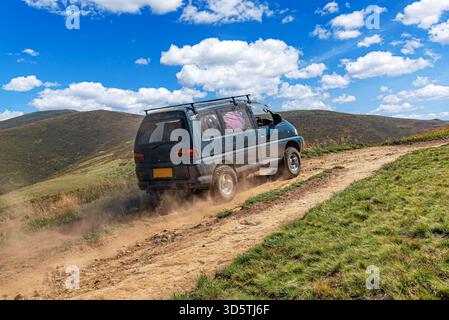 Ein Kleinbus mit Allradantrieb fährt schnell eine staubige, unbefestigte Strecke in einer grasbewachsenen, bergigen Landschaft hinauf Stockfoto