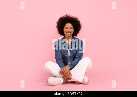 Lächelnde schwarze Frau, die im Kreuz auf dem Boden sitzt und entspannt und glücklich aussieht Stockfoto