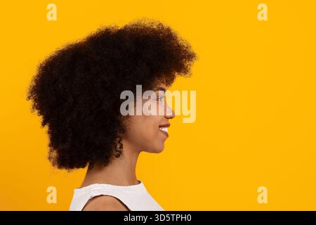 Profilporträt einer jungen schwarzen Frau, die im Atelier lächelt, vor gelbem Hintergrund Stockfoto