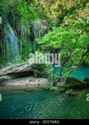 Ruhiger, versteckter Wasserfall, der über moosige Felsen in einen hellen türkisfarbenen Pool stürzt, umgeben von üppigen, sonnendurchfluteten grünen Wäldern. Friedliche Natur esca Stockfoto