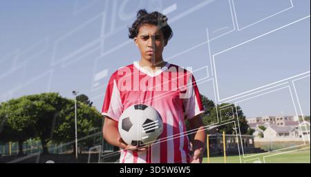 Stehender, erwachsener Fußballspieler, der Fußball auf einem grasbewachsenen Feld hält, in rot-weißem Trikot Stockfoto