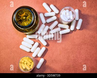 Verschiedene Pillen, Kapseln & Medizin - Sortiment an pharmazeutischen Pillen, weißen Kapseln und gelben Softgels auf einer strukturierten rötlich-braunen Oberfläche, s Stockfoto