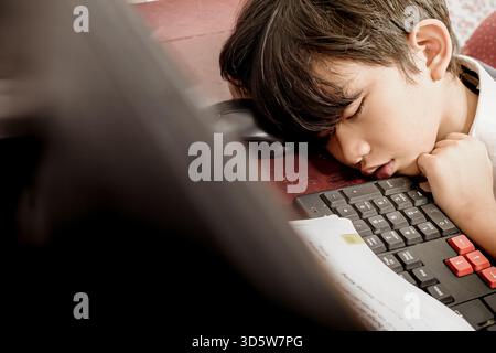 Südostasiatischer Junge schlief ein, als er nach der Schule seine Hausaufgaben am Computer machte Stockfoto