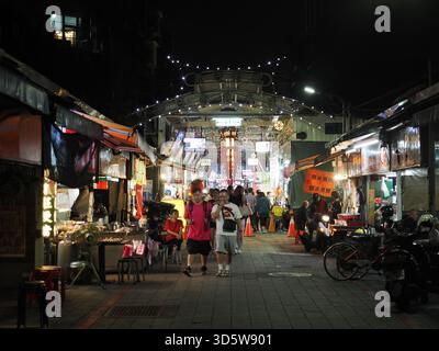 Taipei, Taiwan - 17. November 2024: Besucher schlendern durch die überdachte Gasse des Huaxi Street Night Market, vorbei an Imbissständen und Sitzbereichen. Stockfoto