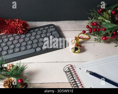 Festlicher Arbeitsbereich mit Tastatur – Eine moderne, dunkle Tastatur, umgeben von festlichem rotem Lametta, goldenen Glocken und grünen Kiefernzweigen in rustikalem Ambiente Stockfoto