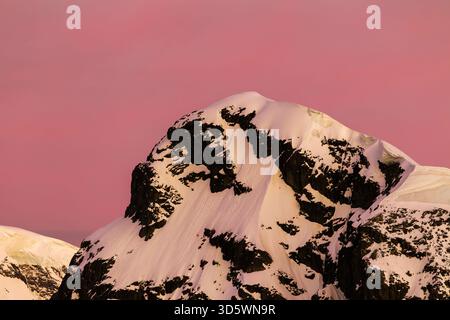 Ein schneebedeckter Berggipfel mit einem rosa Himmel während des Sonnenuntergangs in der Antarktis. Stockfoto