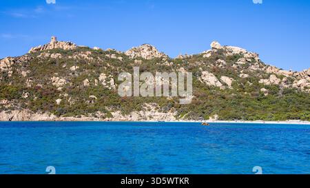 Die Bucht von Roccapina mit ihrem wunderschönen türkisfarbenen Wasser vom Meer aus gesehen, mit dem Wachturm und liegendem Löwen auf dem Hügel in der Sonne Stockfoto