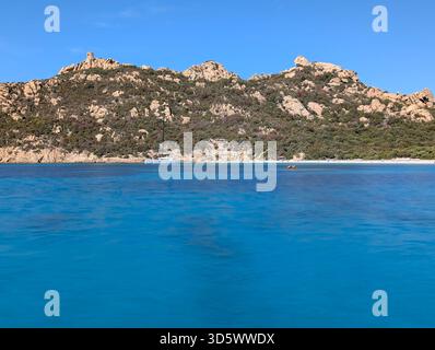 Die Bucht von Roccapina mit ihrem wunderschönen türkisfarbenen Wasser vom Meer aus gesehen, mit dem Wachturm und liegendem Löwen auf dem Hügel in der Sonne Stockfoto