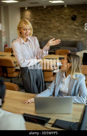 Zwei Frauen führen in einem stilvollen Büro mit bequemen Sitzgelegenheiten eine freundliche Diskussion. Eine Geste bewegt sich animiert, während die andere aufmerksam zuhört. T Stockfoto