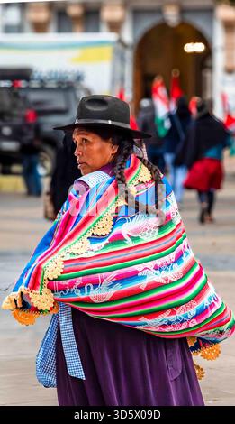 Bolivianische Frau in traditioneller Andenkleidung mit farbenfrohem Manta und geflochtenem Haar, die in einer städtischen Straße in Bolivien spaziert. Stockfoto