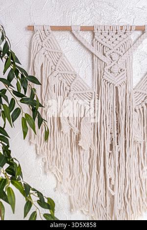 Handgefertigte Makramee-Wandbehang mit langen Fransen und geometrischen Knoten. Trendiges Boho-Dekor, handgefertigtes Kunsthandwerk, natürliches, gemütliches Ambiente in moderner Einrichtung. Stockfoto