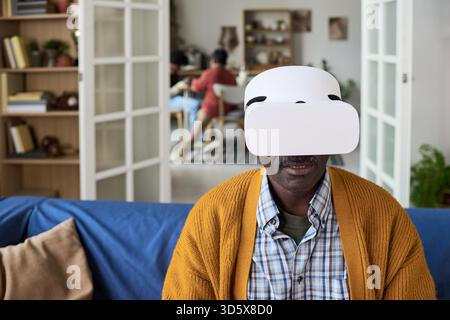 Reifer Schwarzer Mann mit Virtual Reality-Headset im modernen Wohnzimmer Stockfoto