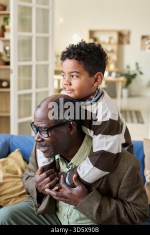 Senior Black man trägt Black Boy auf den Schultern und lächelt drinnen Stockfoto
