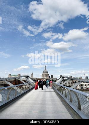 London, Großbritannien - 22. September 2025: Eine geschäftige Gruppe schlendert entlang einer modernen Brücke in London mit St Pauls Cathedral und blauem Himmel. Stockfoto