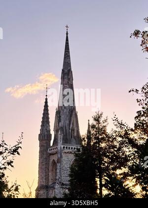 London, Großbritannien - 22. September 2025: Ein dramatischer Sonnenuntergang über einer historischen gotischen St. Mary Abbots Church mit hohen Türmen und umliegendem Laub. Stockfoto