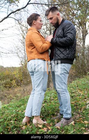Ein Paar steht eng zusammen in einer malerischen Umgebung im Freien, umgeben von Grün und Herbstlaub. Ihr Blick ist voller Zuneigung und in sich Stockfoto