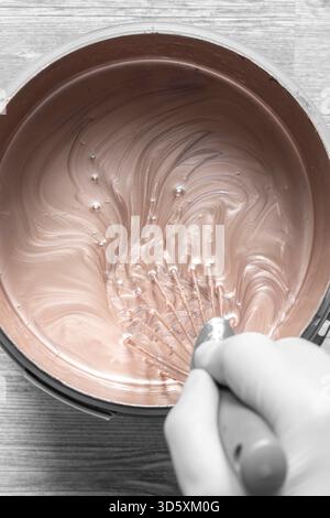 Person, die Goldfarbe in einem Kunststoffbehälter mit einem Metallbesen mischt. Dekorationskonzept Do IT Yourself für Zuhause. Stockfoto