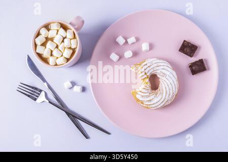 Stillleben eines gebissenen Kuchens auf einem rosafarbenen Teller, Besteck und eine Tasse Kakao mit Marshmallows. Selektiver Fokus, horizontale Ausrichtung Stockfoto
