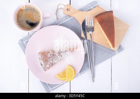 Nahaufnahme von oben auf zwei Stück Kuchen auf einem rosafarbenen Teller und ein Schneidebrett mit Messer und Gabel auf einer gefalteten Leinenserviette und einer Tasse mit Kaffee. Homem Stockfoto
