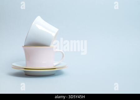 Zwei Porzellantassen und Untertassen für Tee oder Kaffee in blauen und rosa Farben stehen auf blauem Hintergrund. Pastellfarben. Selektiver Fokus. Kopierbereich Stockfoto