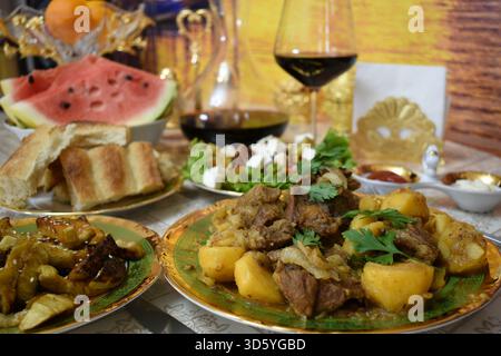 Geschmortes Lamm mit Kartoffeln und Auberginen, serviert mit Rotweinkaraffe, Wassermelone und Früchten Stockfoto