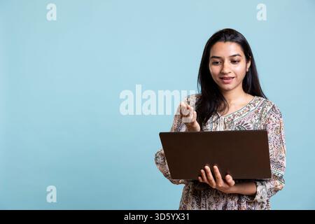 Fröhliche Person, die mit Freunden bei einer Videokonferenz tratscht und sich vor dem Hintergrund des Studios posiert. Glückliche, entspannte Frau, die sich mit ihren Mädchen verbündet, nehmen Sie an Online-Videogesprächen auf dem Laptop teil. Stockfoto