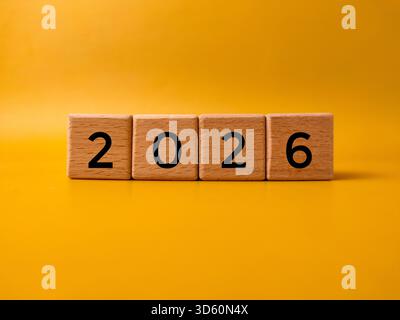 Das Bild zeigt vier Holzblöcke auf gelbem Hintergrund, die das Jahr 2026 darstellen. Stockfoto