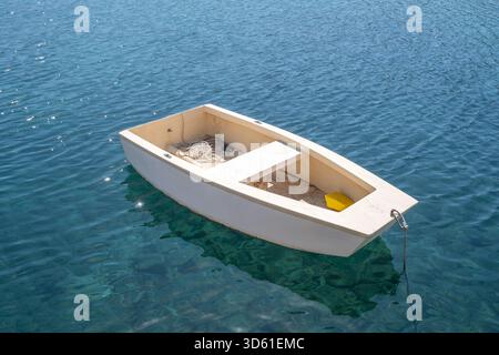 Kleines weißes Ruderboot, das auf ruhigem türkisfarbenem Wasser unter hellem Mittagssonnenlicht treibend, friedliche Szene Stockfoto
