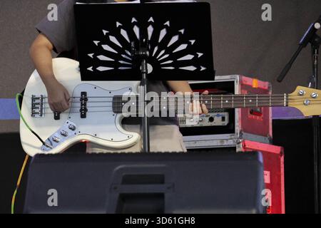 Nahaufnahme eines fokussierten Musikers, der weiße E-Bass-Gitarre auf der Bühne spielt. Leidenschaftliche Auftritte bei Konzerten oder Festivals mit professioneller Musik e Stockfoto