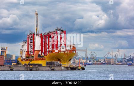 Schwerlastschiff im Industriehafen Gdynia, Polen, mit roten Portalkränen angedockt Stockfoto
