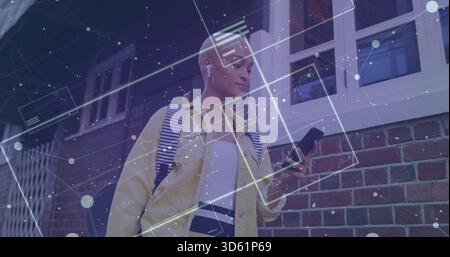 Frau in gelber Jacke, die das Telefon mit Ohrstöpseln und digitaler Überlagerung an der Wand ansieht Stockfoto